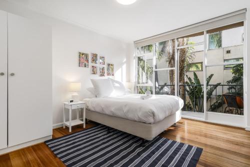 a white bedroom with a bed and a large window at Seaside 1-Bed Stay Near Cafés & Attractions in Melbourne