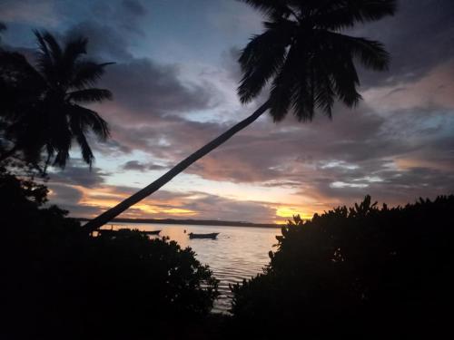 a sunset with a boat in the water with palm trees at Mahina Lodge in Mafana