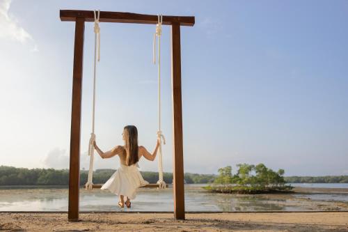a woman in a white dress swinging on a wooden swing at Pramana Nusa Ceningan in Nusa Lembongan