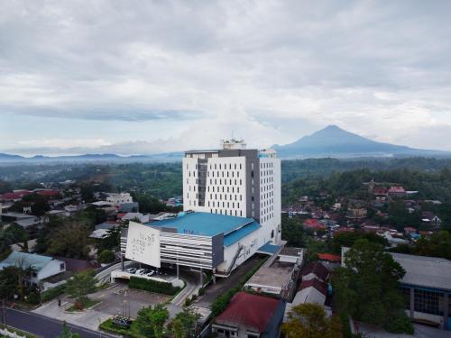 a tall white building with a mountain in the background at Luwansa Hotel and Convention Center Manado in Manado