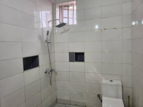 a white tiled bathroom with a shower and a toilet at Wuse 2 Studios- City Center in Abuja