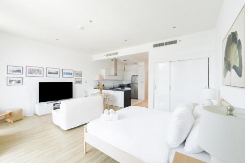 a white living room with a white couch and a tv at Stylish Studio in Al Barza hosted by Voyage in Abu Dhabi