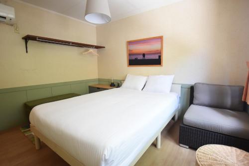 a bedroom with a white bed and a chair at Inn Between Waves in Shimoda