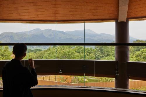 a person looking out of a large window at mountains at Hotel Yumeshizuku in Minami Aso