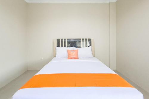 a white bed with an orange pillow on it at Sans Hotel Bliss Pekanbaru in Sultan Syarif Kasim II International Airport