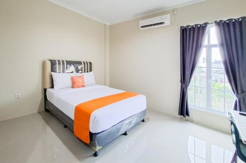 a bedroom with a bed with an orange pillow and a window at Sans Hotel Bliss Pekanbaru in Sultan Syarif Kasim II International Airport