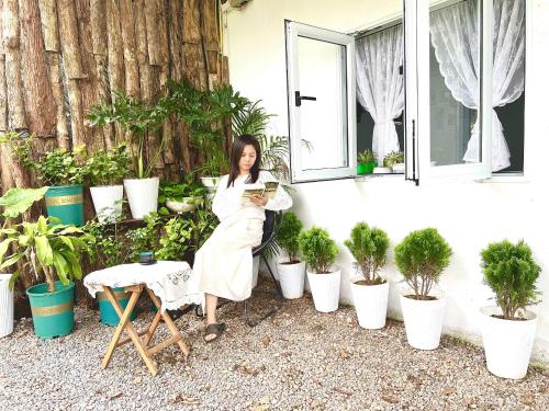 a woman reading a book in front of plants at Poong's Garden Mộc Châu in Mộc Châu