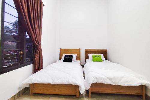 two twin beds in a room with a window at Urbanview Hotel Syariah at Glory Guest House Kota Baru in Sultan Thaha Airport