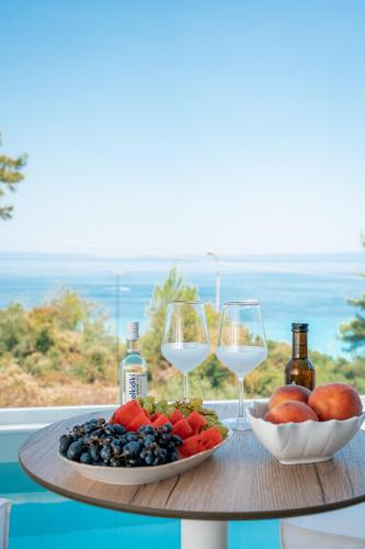 a table with two glasses of wine and a plate of fruit at Gloria Luxury Suites in Kallithea Halkidikis
