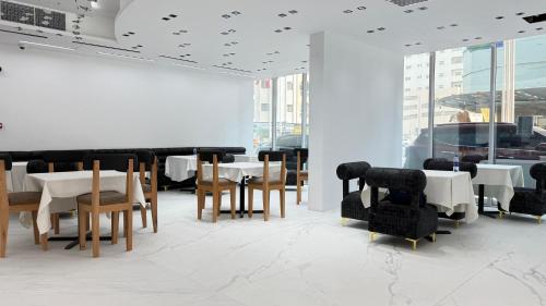 a dining room with white tables and chairs and windows at Royal Tulip Dancenter Suites Sharjah in Sharjah