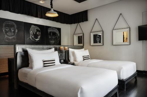 two white beds in a room with pictures on the wall at Shinta Mani Angkor in Siem Reap