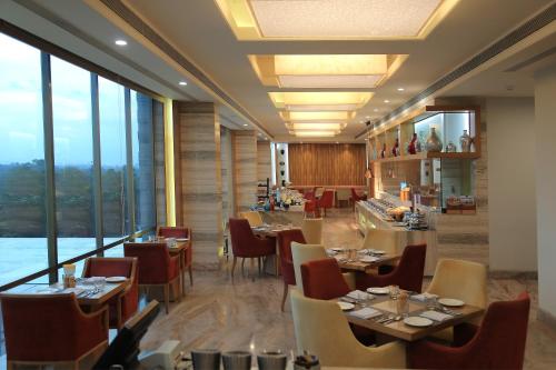 a restaurant with tables and chairs and large windows at Efcee Sarovar Premiere Bhavnagar in Bhavnagar