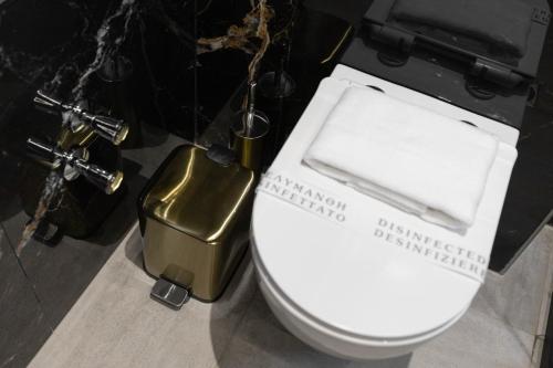 a bathroom with a white toilet with a gold trash can at Calma Luxury Suites in Paralia Dionysiou