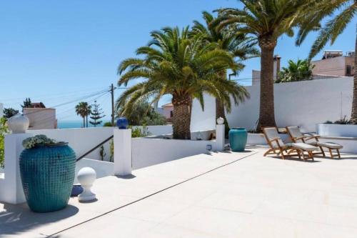 a patio with chairs and palm trees and a white fence at Riad Salt Pool Bliss Apartamentos in Torremolinos