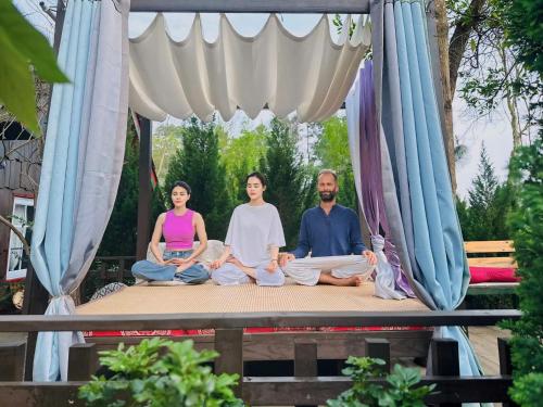 a group of three people sitting in meditation on a stage at Khu nghỉ dưỡng Ba Hạt Dẻ in Sóc Sơn
