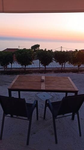 a wooden picnic table and two chairs in front of a sunset at Sun Meets Sea in Athanion
