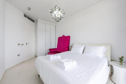 a white bedroom with a pink chair and a bed at Villa Belle Azure in Dhërmi