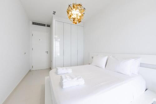 a white bedroom with a white bed and a chandelier at Villa Belle Azure in Dhërmi