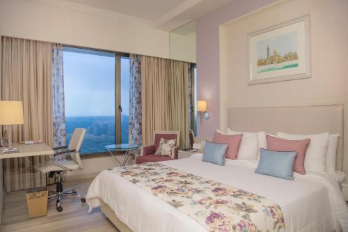 a hotel room with a large bed and a desk and window at Efcee Sarovar Premiere Bhavnagar in Bhavnagar