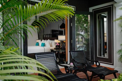 two chairs and a bed on a porch with plants at Shinta Mani Angkor in Siem Reap