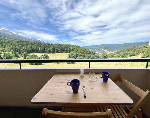 a wooden table with two cups on a balcony with a view at Métamorphose au sommet, studio au pied des pistes in Villard-de-Lans