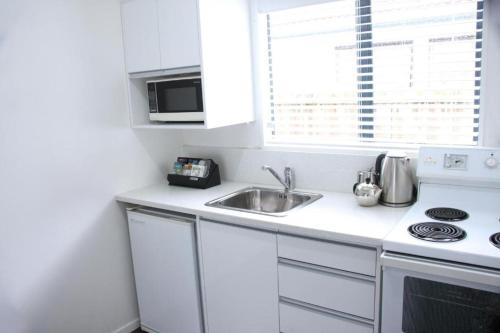a white kitchen with a sink and a microwave at Camelot On Ulster in Hamilton