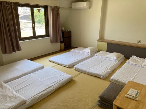 a room with four beds in it with a window at J-Hoppers Beppu Guesthouse ジェイホッパーズ別府ゲストハウス in Beppu