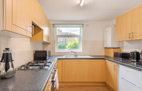 a kitchen with wooden cabinets and a stove top oven at Elegant 2BR Ground-Floor Teddington Flat Modern Comfort in Kingston upon Thames