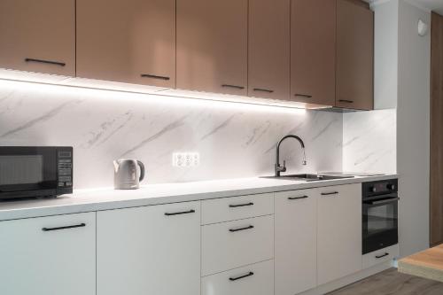a kitchen with white cabinets and a sink and a microwave at Symphony City Square Aparthotel in Wrocław