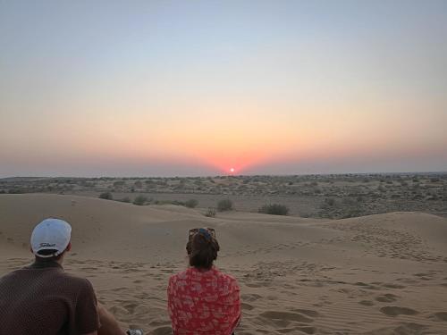 a man and a woman sitting in the desert watching the sunset at Tofu Guesthouse - Fort View in Jaisalmer