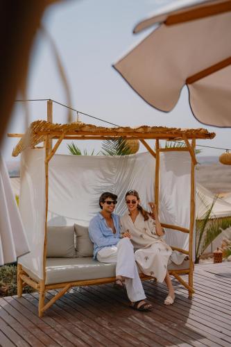 a man and woman sitting on a swing on a beach at Mia Agafay Resort in El Karia