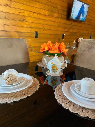 a table with two plates and a vase with orange flowers at Chalé Vô Nono in Barracão