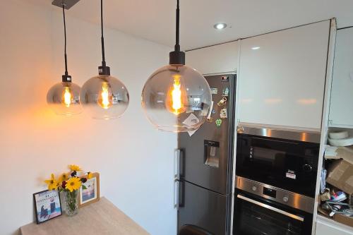 a kitchen with three pendant lights and a refrigerator at Sunset View 2BR Apartment - Beautiful London View & Free Parking in London