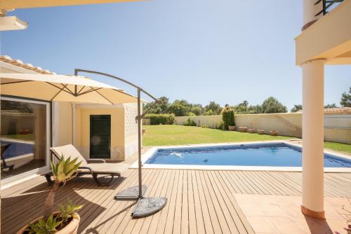 a patio with a swimming pool and an umbrella at São Pedro do Estoril Villa By Hosty in Parede