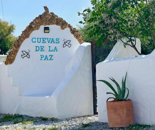 a white fence with a sign in front of a plant at Cuevas de la Paz - Cave House Holidays in Los Carriones