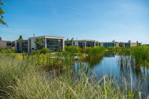 a building next to a body of water with tall grass at Marina Strandbad Chalet Inselperle mit Zaun & AirCo Nr 84 in Olburgen
