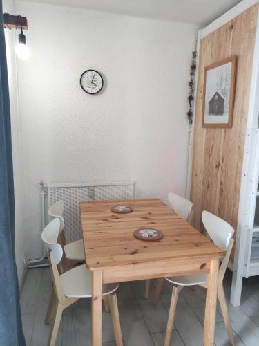 une table en bois avec des chaises blanches et une horloge sur le mur dans l'établissement Résidence Béro Bisto Studio 4 pers la Mongie Grand Tourmalet, à Bagnères-de-Bigorre
