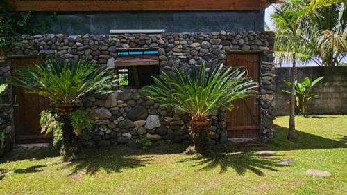 two palm trees in front of a stone building at TAHITI ITI - Saltwater Family Huts in Teahupoo