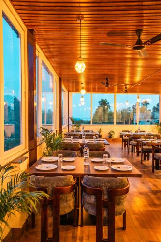 a restaurant with tables and chairs and large windows at Tripli Hotels Ganga Heaven Rishikesh - Laxman Jhula in Rishīkesh