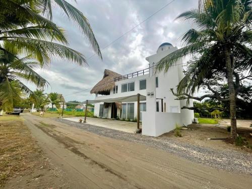 a white building with a thatched roof on a dirt road at Villa Almendro - 4 habitaciones in Iztapa