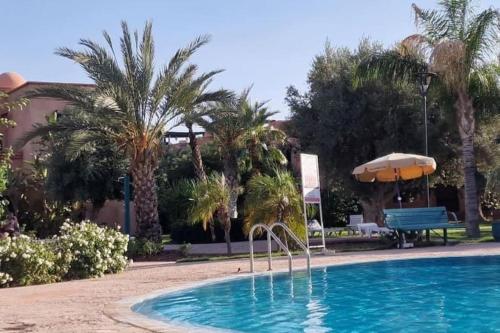 a swimming pool with an umbrella and palm trees at Dar Hegoa Villa Soleil et Chaleureuse in Marrakech