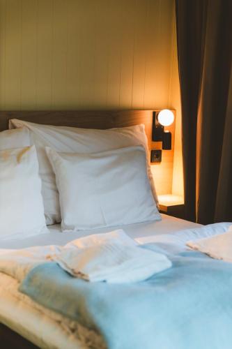 a bed with white sheets and pillows and a lamp at Skata Hotel Henningsvær in Henningsvær