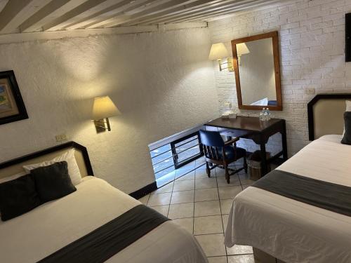 a hotel room with two beds and a desk with a mirror at Hotel Del Portal, Puebla in Puebla