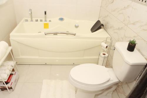 a white bathroom with a toilet and a bath tub at Nyla's Charmed Oasis in Portmore