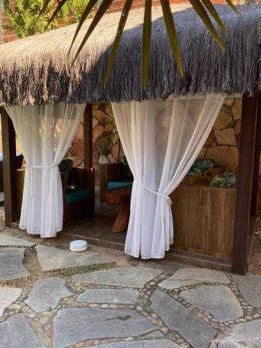 a straw hut with curtains and a thatched roof at Pousada Aliany Lôbo in Pirenópolis