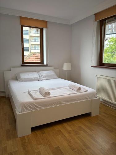 Cama blanca en habitación con 2 ventanas en Teo Apartment, en Pristina