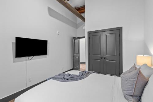 a white bedroom with a bed and a tv on a wall at Brick & Bed Riverfront Lofts, PC 101 in Saint Louis