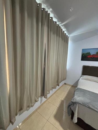 Un dormitorio con cortinas beige y una cama. en Suíte confortável e espaçosa, en Goiânia