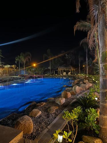 a pool at night with palm trees and blue water at ÓRGANOS BEACH bungalows & suites in Los Órganos