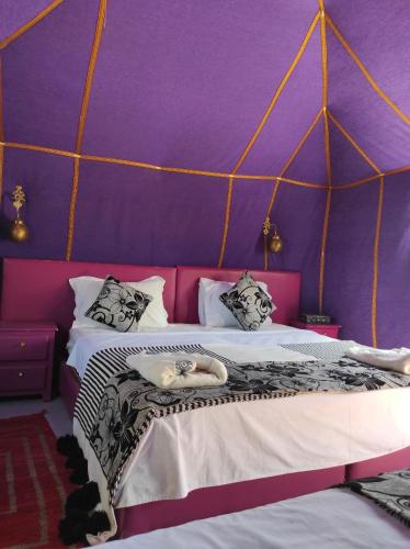 a bedroom with a bed with a purple wall at Merzouga Desert Experience Camp-Erg Chebbi Sunset & Camel Ride in Merzouga